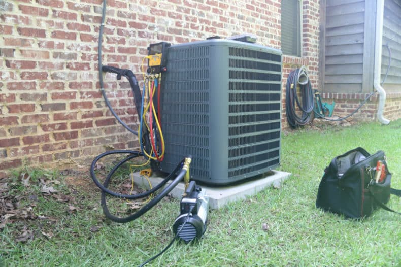 A green air conditioner sitting outside of a brick building.