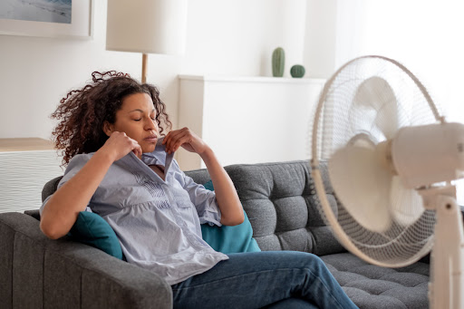 A woman sitting on top of a couch near a fan.