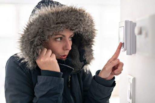 A woman in winter coat adjusting temperature on thermostat.