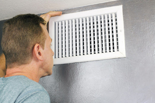 A man looking at an air vent with his hand on it.
