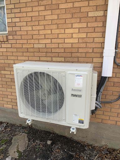 A white air conditioner mounted to the side of a brick wall.