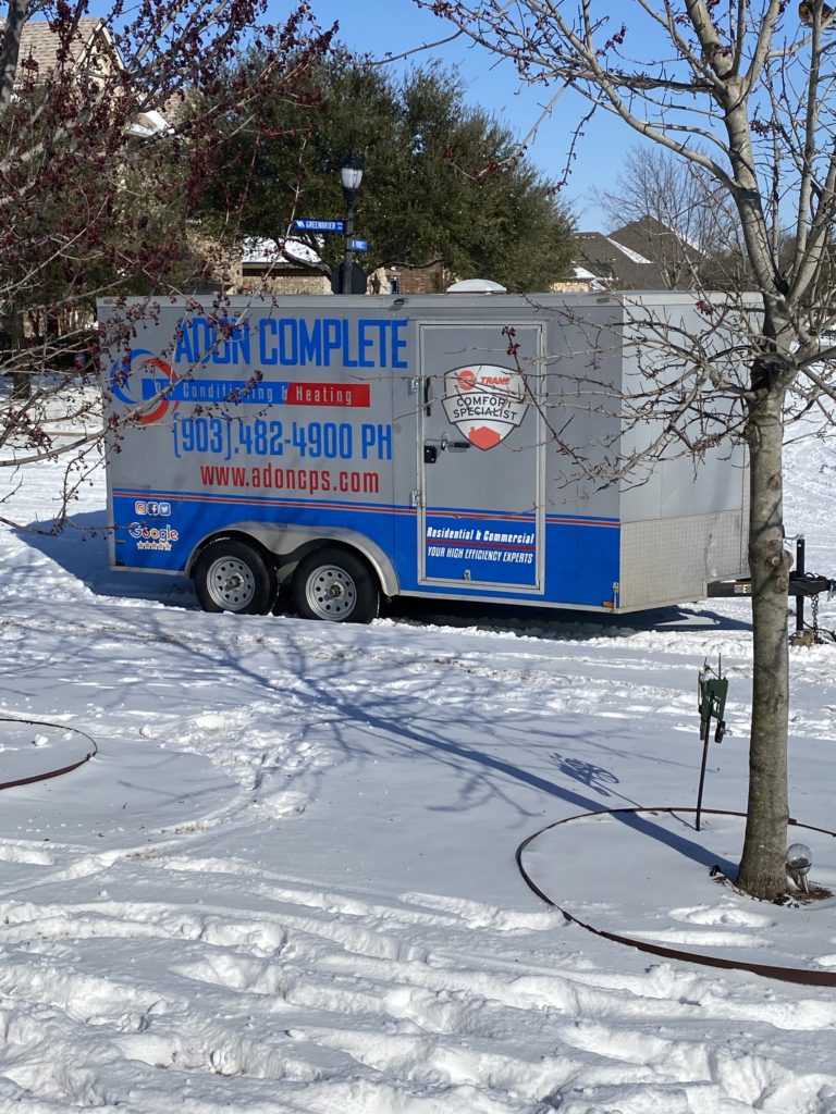 A trailer is parked in the snow near a tree.