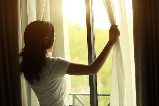 A woman opening up the curtains in her window.