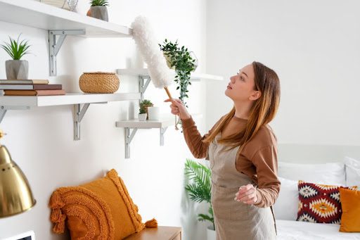 A woman is dusting the shelves in her home.