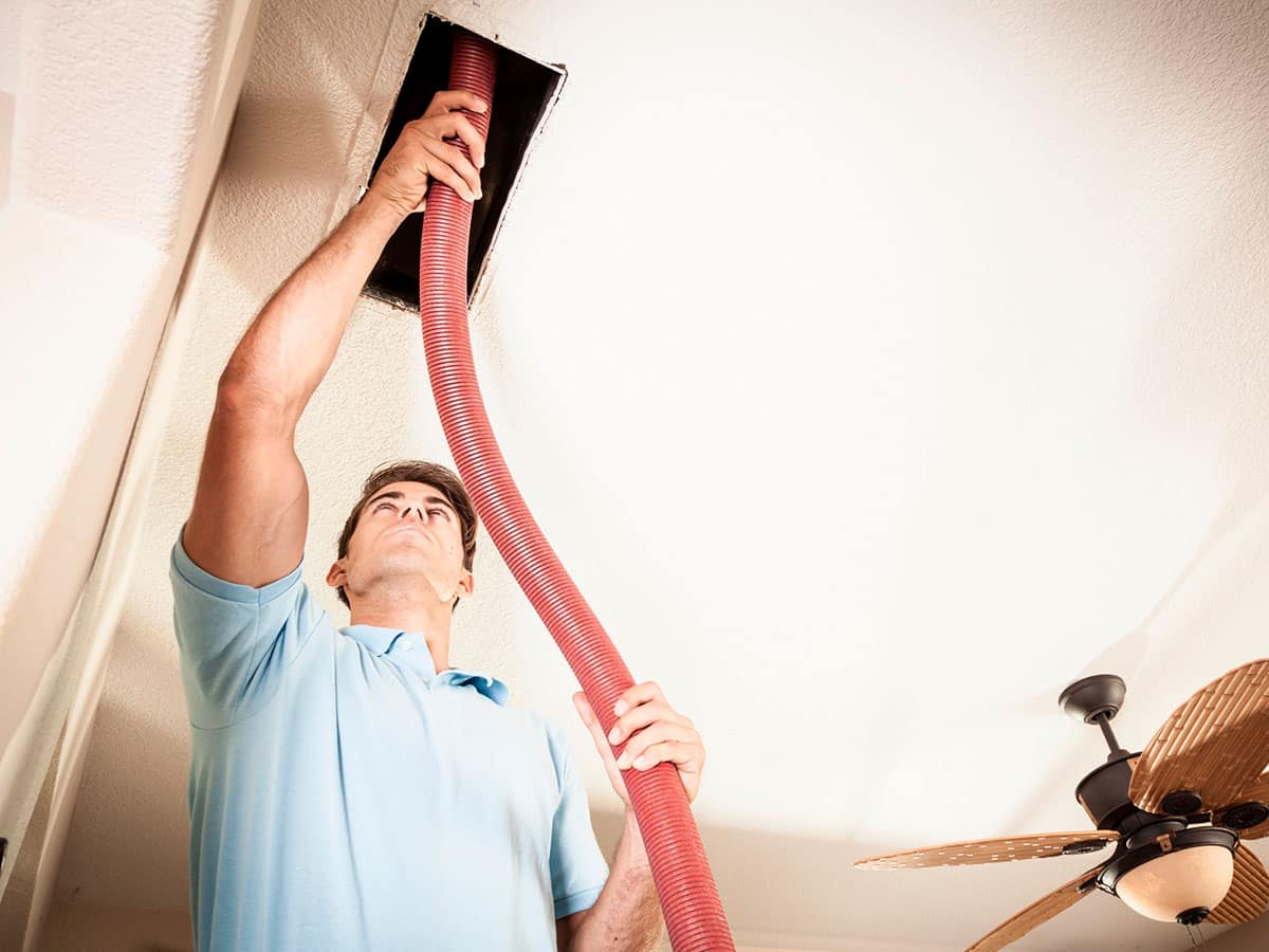 A man holding a red hose over the vent of an air duct.