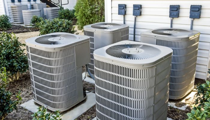 A group of four air conditioners sitting outside.